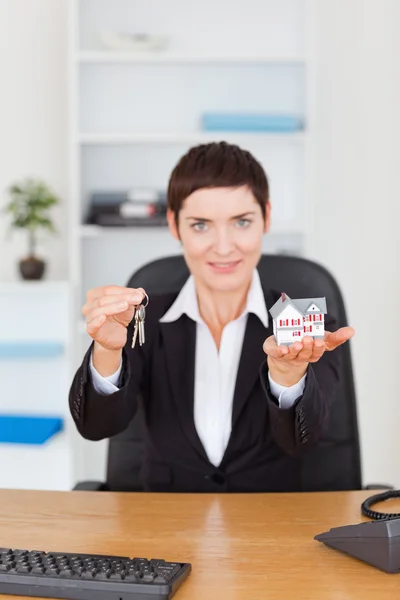 Portrait of a businesswoman showing a miniature house and a key — Stock Photo, Image