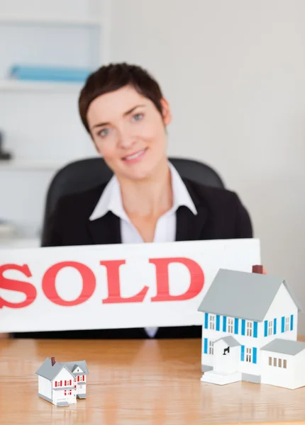 Portrait of a real estate agent with a sold panel and houses min — Stock Photo, Image