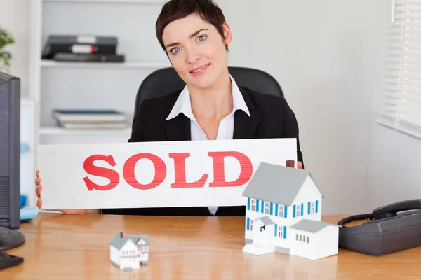 Agente inmobiliario femenino con un panel vendido y casas en miniatura — Foto de Stock