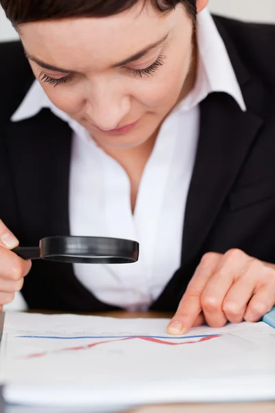 Portrait of a woman looking at a chart with a magnifying glass — Stock Photo, Image