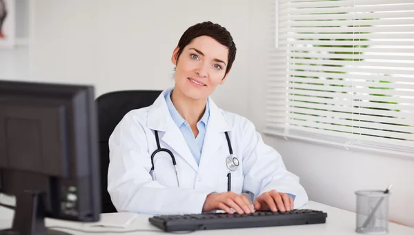 Leende läkare att skriva med hennes dator — Stockfoto