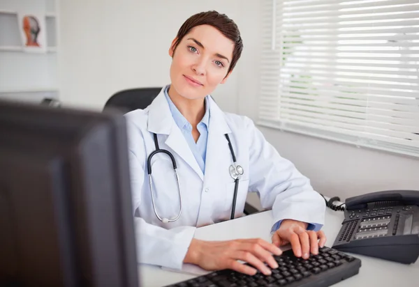 Bonito médico feminino digitando com seu computador — Fotografia de Stock