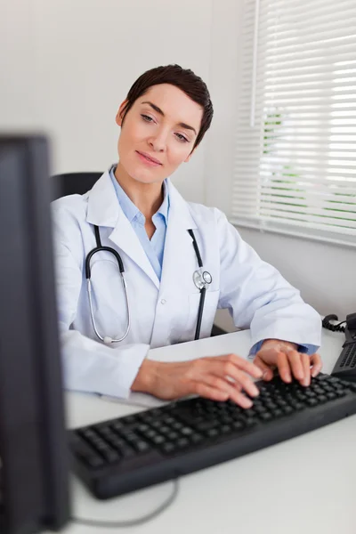 Portrét okouzlující ženského lékaře psaní s počítačem — Stock fotografie