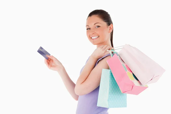 Mujer atractiva con una tarjeta de crédito sosteniendo bolsas de compras mientras — Foto de Stock