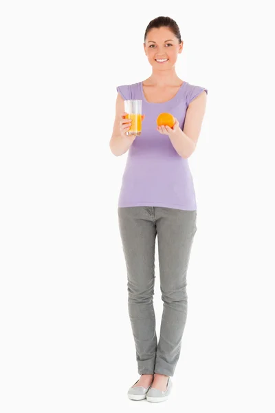 Ελκυστική γυναίκα, κρατώντας ένα πορτοκάλι και ένα ποτήρι χυμό πορτοκαλιού — Φωτογραφία Αρχείου