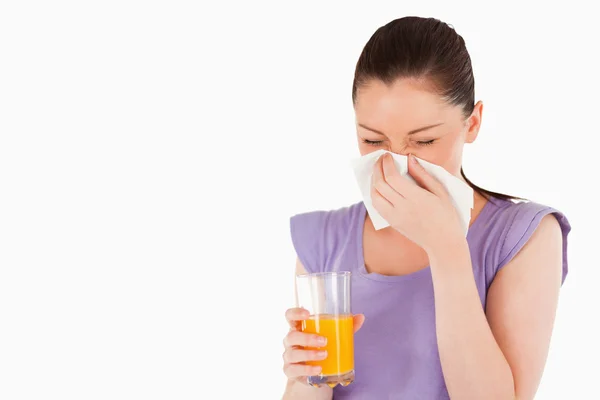 Good looking woman holding a glass of orange juice and sneezing — Stock Photo, Image