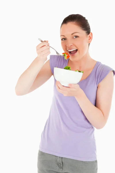 Mulher bonita comendo uma tigela de salada enquanto está de pé — Fotografia de Stock