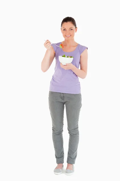 Mujer encantadora comiendo un tazón de ensalada mientras está de pie — Foto de Stock