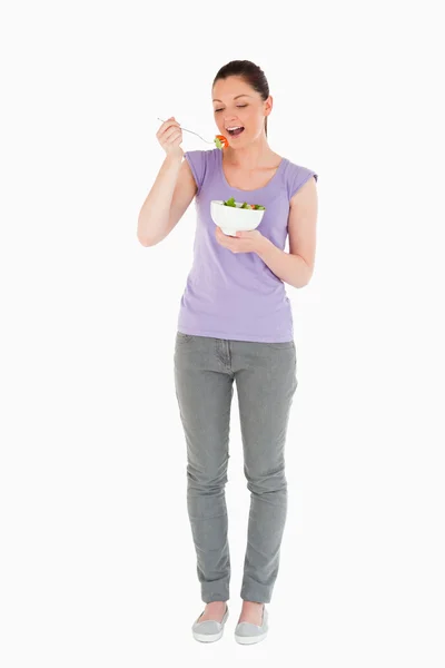 Гарненька жінка їсть тарілку салату, стоячи — стокове фото