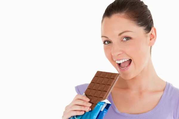 Retrato de uma mulher bonita comendo um bloco de chocolate enquanto — Fotografia de Stock