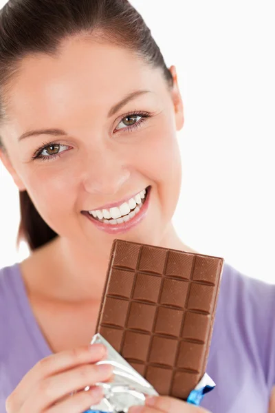 Retrato de una mujer guapa comiendo un bloque de chocolate mientras — Foto de Stock