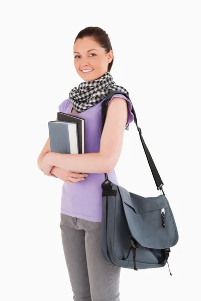 Hermosa estudiante sosteniendo libros y su bolso mientras está de pie —  Fotos de Stock