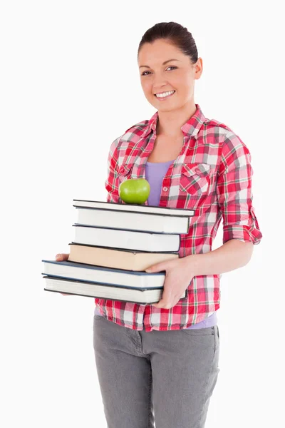 Привлекательная женщина держит и яблоко и книги во время позирования — стоковое фото