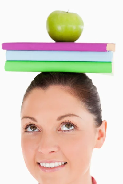 Ελκυστική γυναίκα, κρατώντας ένα μήλο και βιβλία στο κεφάλι της ενώ s — Φωτογραφία Αρχείου