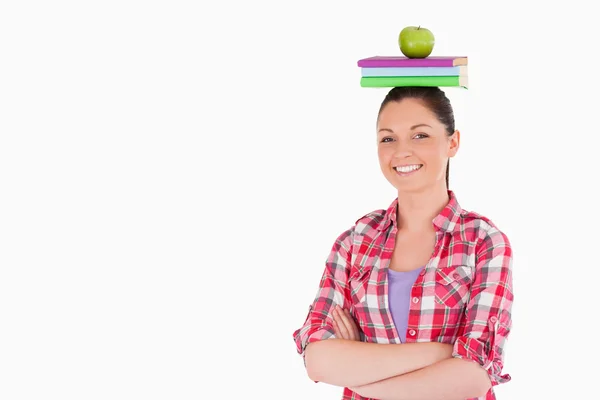Bonita hembra sosteniendo una manzana y libros en su cabeza mientras está de pie —  Fotos de Stock
