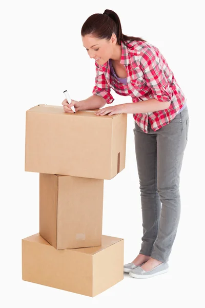 Preciosa mujer escribiendo en cajas de cartón con un marcador mientras st —  Fotos de Stock