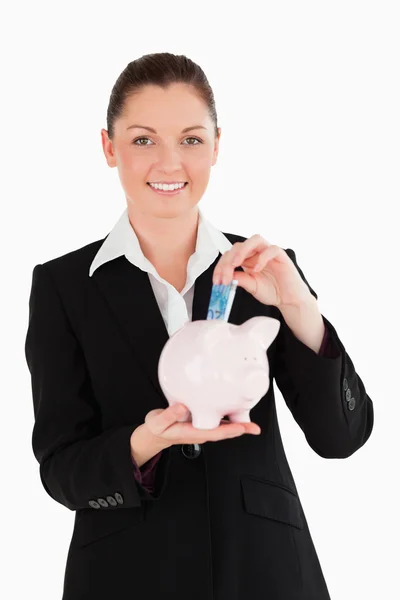 Charming woman in suit inserting a money bill in a pink piggy ba — Stock Photo, Image