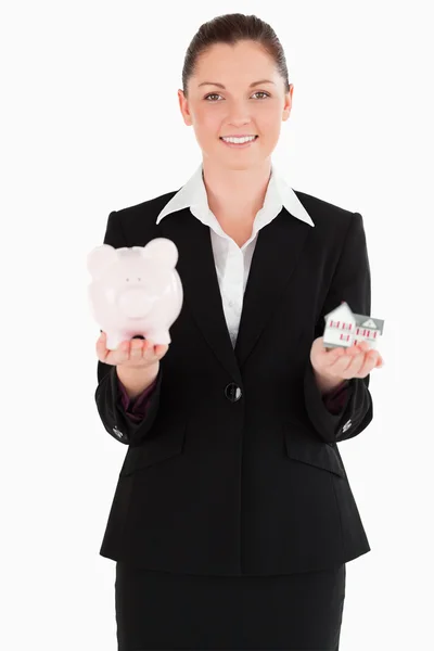 Mulher atraente em terno segurando um banco porquinho e um ho em miniatura — Fotografia de Stock