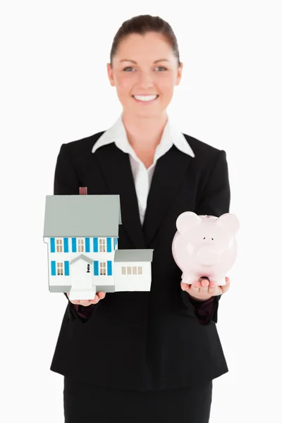 Uroczą kobietą w garniturze gospodarstwa piggy bank i miniaturowe hous — Zdjęcie stockowe