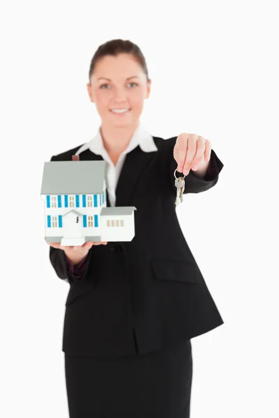 Красивая женщина в костюме держит ключи и миниатюрный дом — стоковое фото