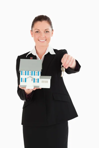 Mulher atraente em terno segurando chaves e uma casa em miniatura — Fotografia de Stock