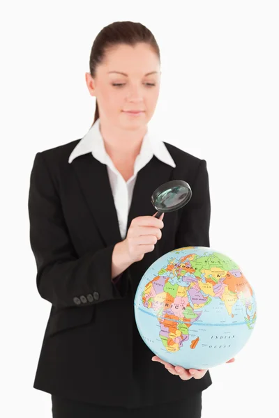 Good looking female in suit holding a globe and using a magnifyi — Stock Photo, Image