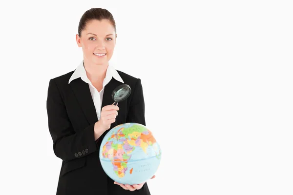 Pretty female in suit holding a globe and using a magnifying gla — Stock Photo, Image