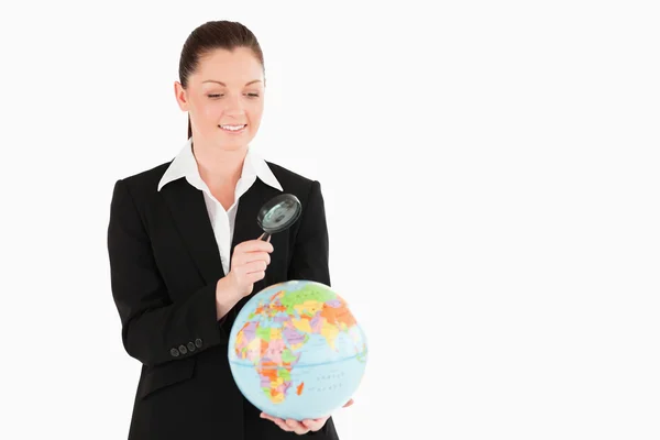 Cute vrouw in pak een globe bedrijf en met behulp van een vergrootglas — Stockfoto