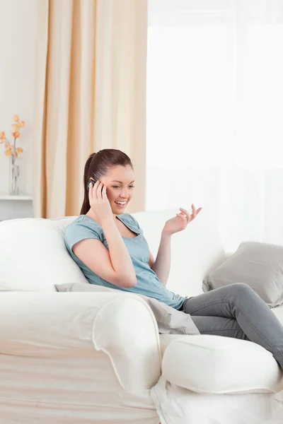Underbara kvinna på telefonen medan du sitter på en soffa — Stockfoto