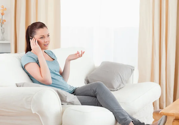 Naštvaná žena na telefonu, zatímco sedí na pohovce — Stock fotografie