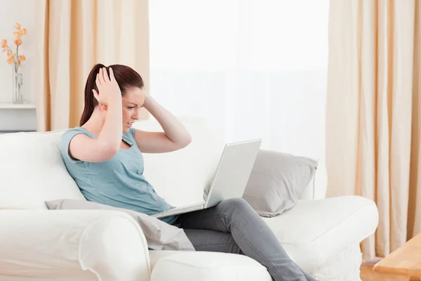 Mulher perturbada jogando com seu computador enquanto se senta em um sofá — Fotografia de Stock