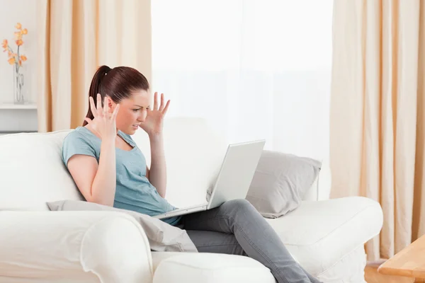Mulher irritada jogando com seu computador enquanto se senta em um sofá — Fotografia de Stock