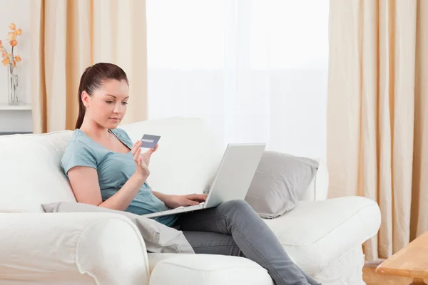 Mujer encantadora haciendo un pago en línea con su tarjeta de crédito mientras —  Fotos de Stock