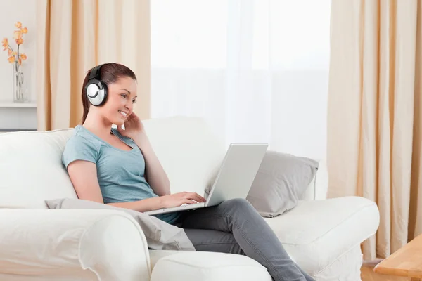Attraktive Frau mit Kopfhörern entspannt mit ihrem Laptop, während — Stockfoto