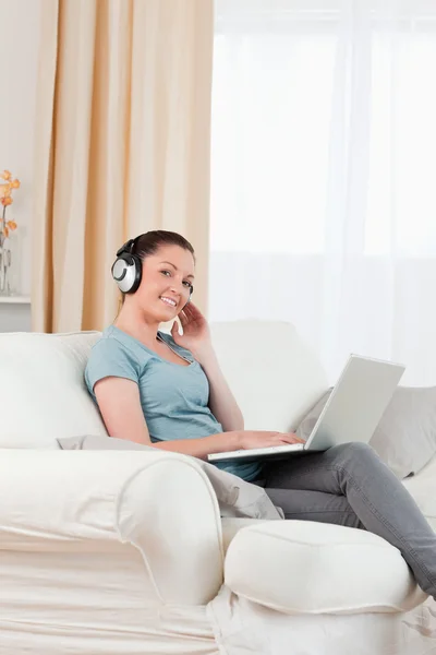 Charmante femme avec écouteurs relaxant avec son ordinateur portable tandis que si — Photo