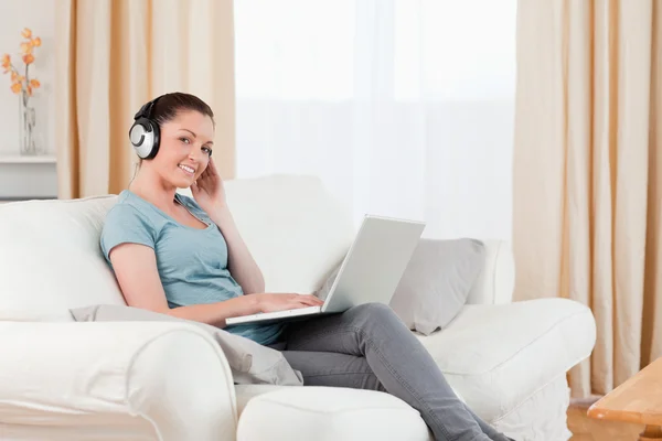 Hübsche Frau mit Kopfhörern entspannt mit ihrem Laptop, während sie sitzt — Stockfoto