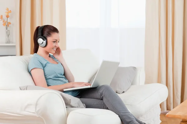 Mulher lindo com fones de ouvido relaxante com seu laptop enquanto si — Fotografia de Stock