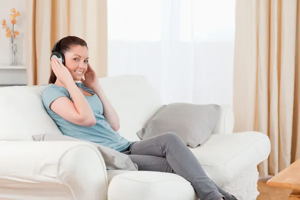 Vacker kvinna avkopplande med hörlurar medan du sitter på en soffa — Stockfoto