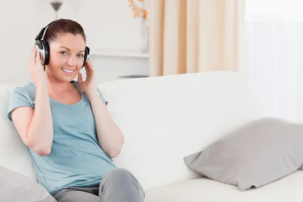 Attraktiv kvinna avkopplande med hörlurar medan du sitter på en sof — Stockfoto