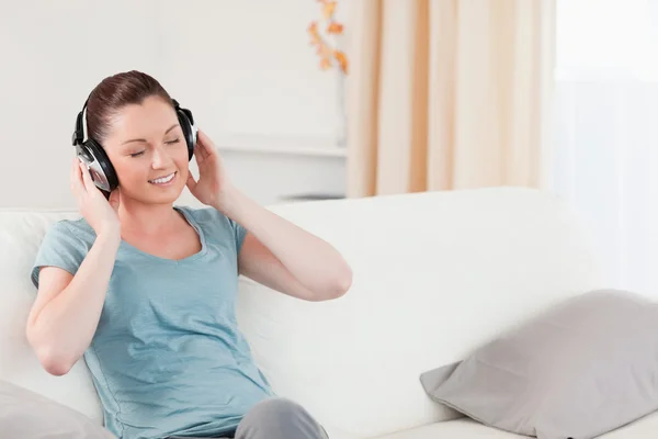 Mujer encantadora relajarse con auriculares mientras está sentado en un sofá —  Fotos de Stock