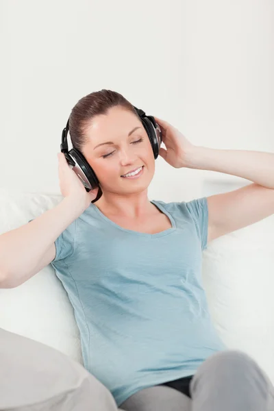 Härlig kvinna avkopplande med hörlurar medan du sitter på en soffa — Stockfoto
