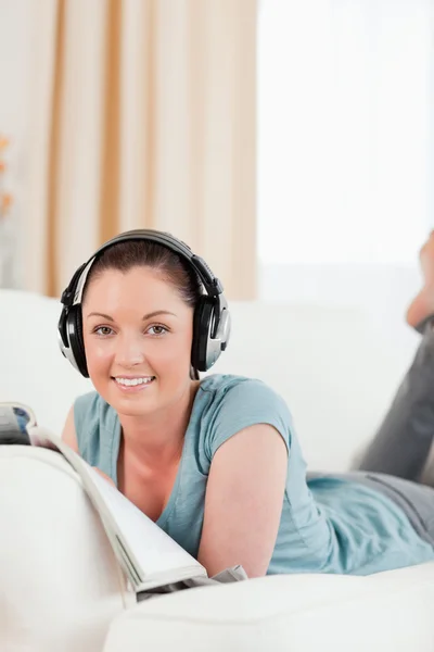 Beautiful woman with headphones reading a magazine while lying o — Stock Photo, Image
