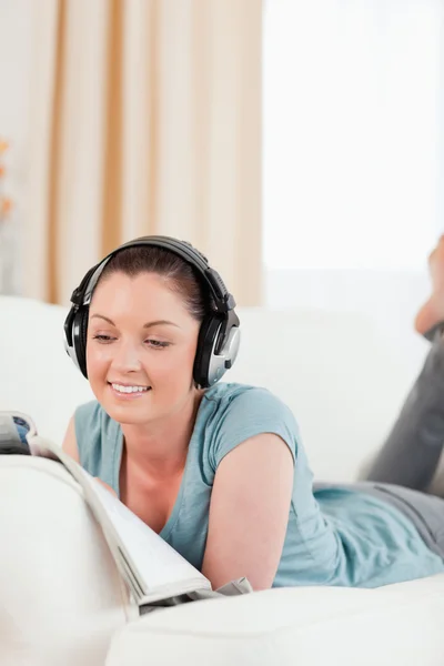 Mulher atraente com fones de ouvido lendo uma revista enquanto mentia — Fotografia de Stock