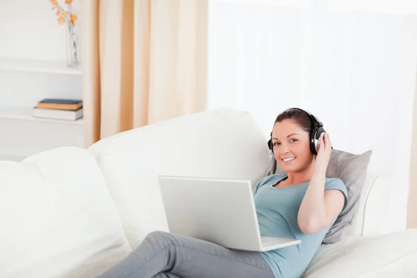 Wunderschöne Frau mit Kopfhörern entspannt auf ihrem Laptop, während lyi — Stockfoto