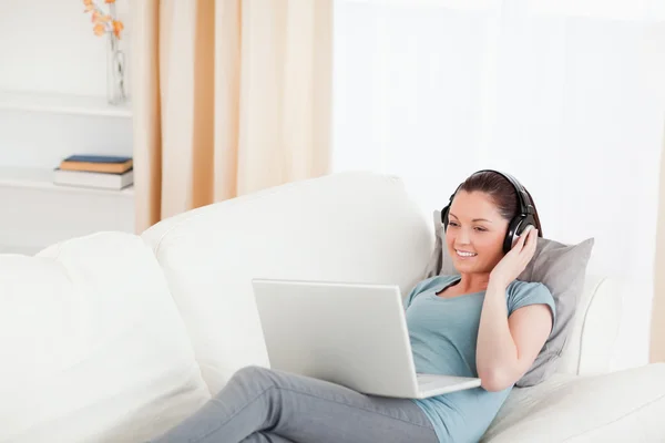 Piękna kobieta z słuchawkami na jej laptopie podczas ly — Zdjęcie stockowe