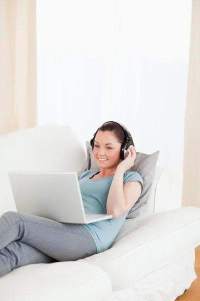 Attraktiv kvinna med hörlurar avkopplande på hennes laptop medan l — Stockfoto