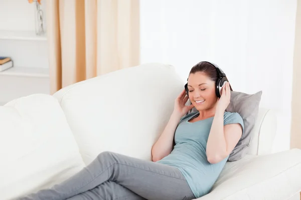 Mulher bonita usando fones de ouvido enquanto deitada em um sofá — Fotografia de Stock