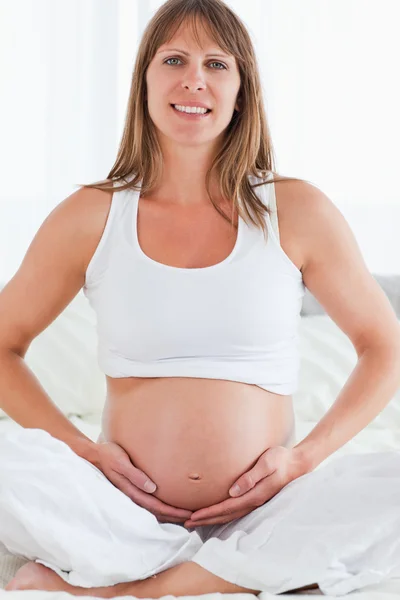 Portrait of a young pregnant female posing while sitting on a be Stock Image