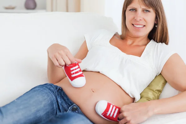 Good looking pregnant female playing with red baby shoes while l — Stock Photo, Image