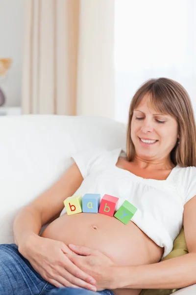 Charming pregnant woman playing with wooden blocks while lying o Stock Photo